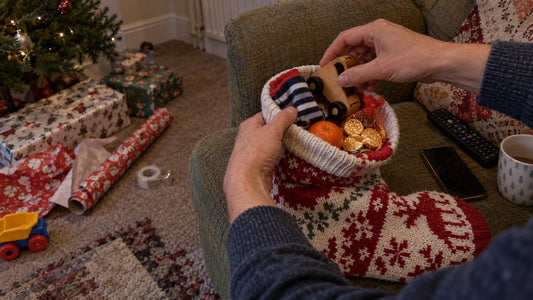 A parent putting a wooden toy car, striped socks, a tangerine and chocolate coins into a knitted Christmas stocking on Christmas Eve